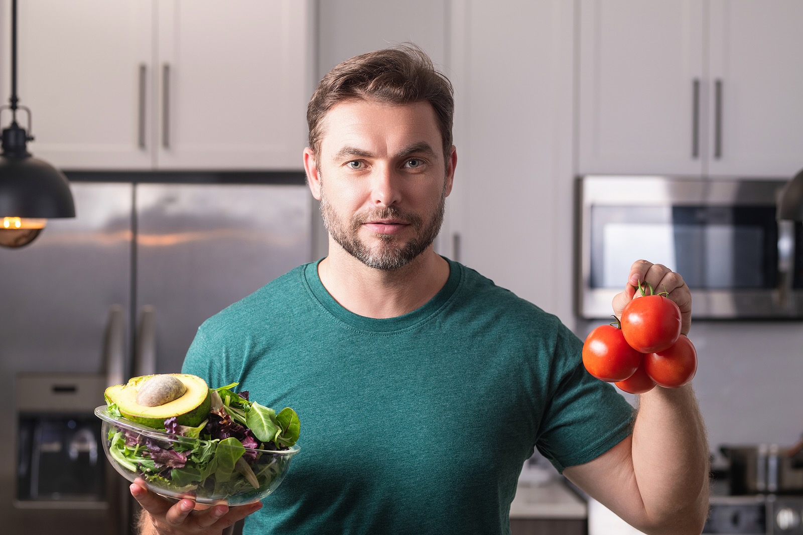 Man in modern kitchen, preparing healthy food alone, cooking salad. Handsome man is preparing fresh vegan salad in the kitchen at home. Healthy food is healthy life.
